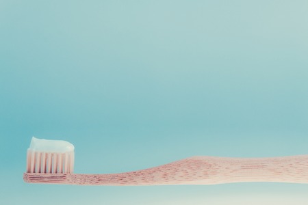 Beige dental brush with white toothpaste on blue white background. Isolated.