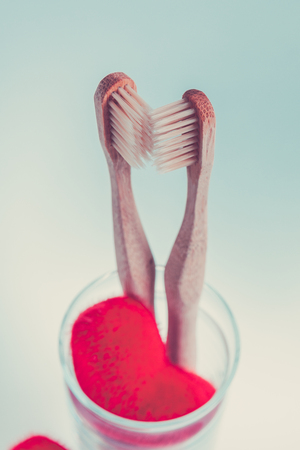 Two beige dental brushes in glass cup with red hearts on blue white background. Isolated.Love. Valentine day.の写真素材