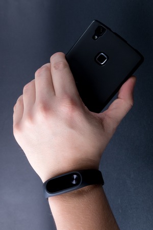 Close up of men's hand with a sports bracelet and smartphone on black