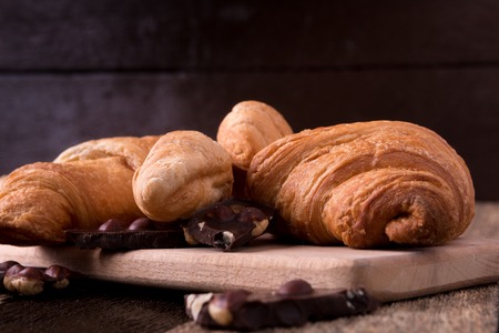 Croissants on board on wooden background. Rustic style. Piece of chocolateの写真素材