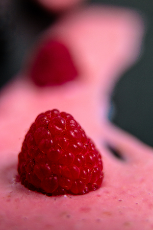 Spilled raspberry smoothie on black table near berry. Close up.