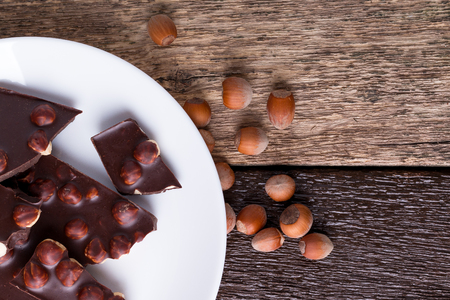 Chocolate pieces with hazelnut nuts on white plate wooden background. Copy space. Top view.の写真素材