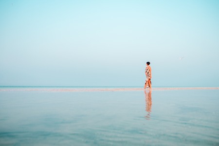 Woman in a floral dress sitting in shallow ocean water. Girl in the sea. looking into the distanceの写真素材