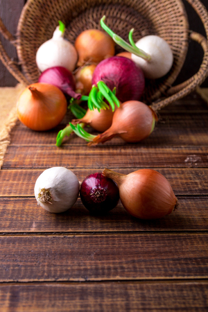 Different onions in basket on wooden background. Rustic style.  Red, white and goldenの写真素材
