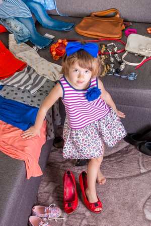 Little girl  wearing  big mother red shoes and bag.  New clothes. Choosing.の写真素材