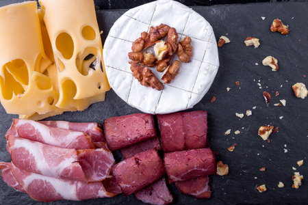 Cheese and meat plate with walnuts on black background. Top viewの写真素材