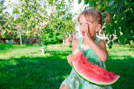 Little blonde with slice of watermelon in summer park. Happy. Screaming, calling.の写真素材