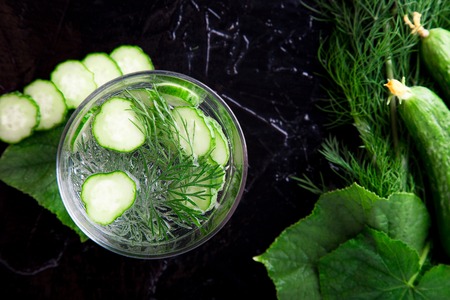 Cucumber water in glass with dill on black background. Detox, diet. Backlight. Top view. Copy spaceの写真素材