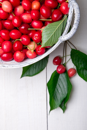 Red cherries in white basket on white wooden background. Cherry close up. Top view.の写真素材