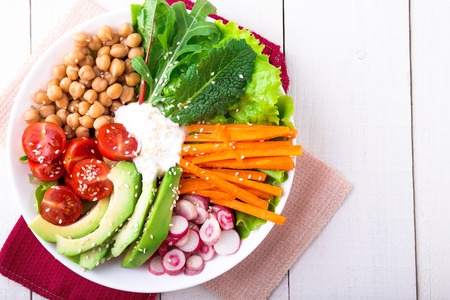 Vegan buddha bowl on white wooden background. Bowl with carrot, lettuce, tomatoes cherry, radish, avocado and chickpea. Vegetarian, healthy, detox food concept. Top viewの写真素材