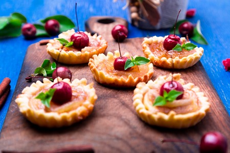 Apple caramel little tarts on wooden board and blue rustic background. French tatin with paradise...