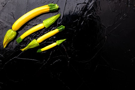 Yellow small zucchinis with flower on black background. Top view.  Frame. Copy spaceの写真素材