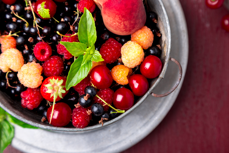 Mix fruit and berries in grey metal bowl on red backgroundの写真素材