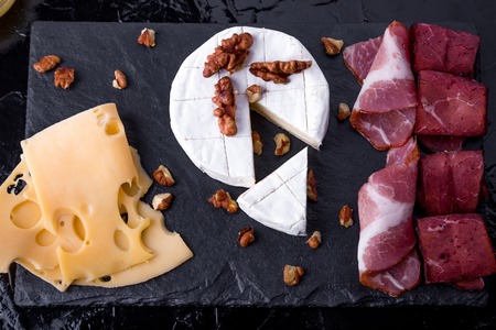 Cheese and meat plate with walnuts on black slate plate background. Top view. Camembert with honey.の写真素材