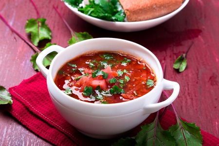 Ukrainian traditional borsch. Russian vegetarian red soup  in white bowl on red wooden background. ...