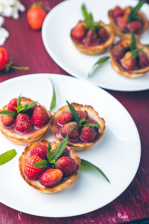 Strawberry tartlet on white plates on  red background. Toned photo. Flower decorated.の写真素材