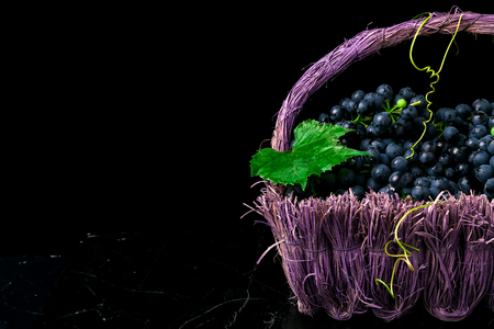 Red wine grapes in voiolet basket on bllack backgroundの写真素材