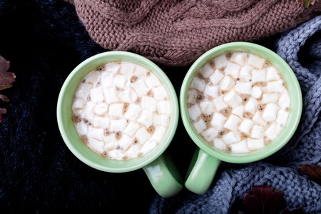 Two cup of coffee or hot chocolate with marshmallow near three knitted grey, black and brown sweater or  knitted blanket. Autumn concept. Christmas. Top view. Warm at homeの写真素材