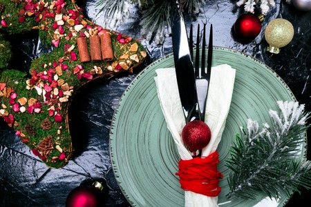 Christmas table place setting. Holidays background. Green plate, knife and fork with christmas decorations on black table. Top viewの写真素材
