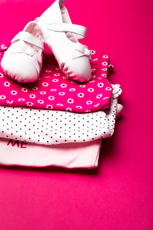 Folded pink bodysuit with shoes on it on minimalistic pink background. diaper for newborn girl. Stack of infant clothing. Child outfit.の写真素材