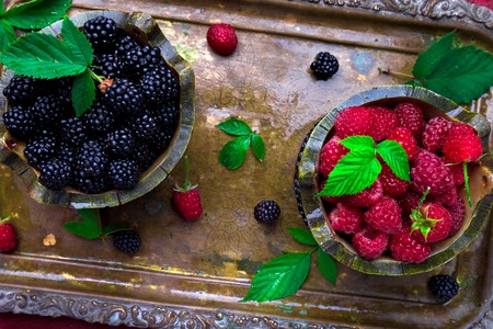Red raspberry and  blackberry with leaf in a basket on vintage metal tray. Top view. 
