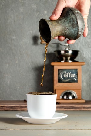 Men Hand Pouring a Cup of Coffee Creating Splash on Wooden Backgroundの写真素材