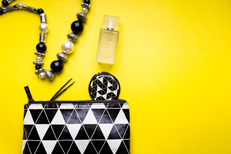 Woman handbag with makeup and accessories on yellow background. Flat lay