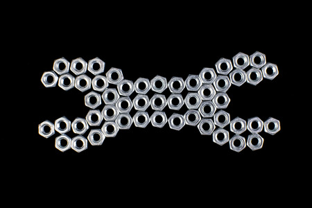 Nut wrench from metal nuts, bolts on black background. Flat lay.