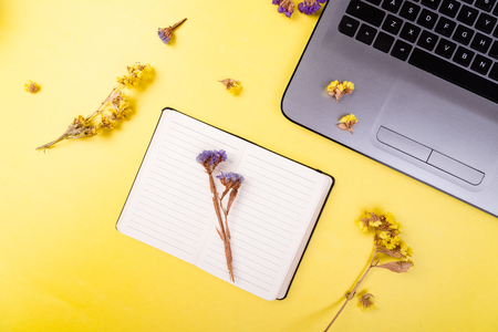 Notebook and flowers for female home or office workplace on yellow background. top view. Copy space.の写真素材