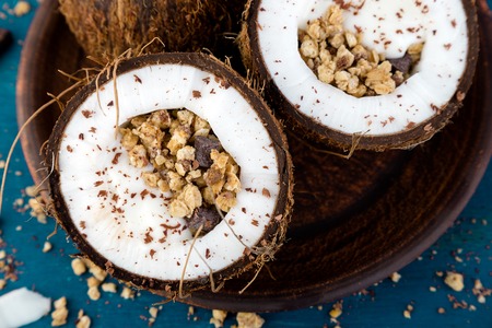 Healthy breakfast in coconut bowl. Yogurt in coconut bowl with coconut flakes, chocolate and granola. Top view, flat lay, overheadの写真素材