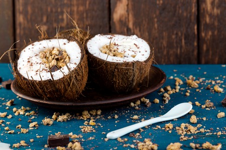 Healthy breakfast in coconut bowl. Yogurt in coconut bowl with coconut flakes, chocolate and granola. Top view, flat lay, overheadの写真素材