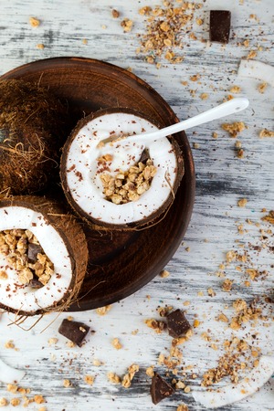 Healthy breakfast in coconut bow on white background. Yogurt in coconut bowl with coconut flakes, chocolate and granola. Top view, flat lay, overheadの写真素材