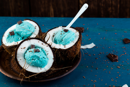 Blue ice cream with chocolate in coconut bowl on wooden background. Summer food. の写真素材