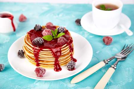 American pancake with jam and frozen raspberry with tea on blue background.の写真素材