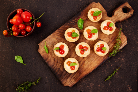 Mini tarts with cherry tomatoes with mozzarella cheese on wooden board. Top view. Copy space.の写真素材