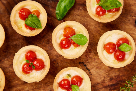 Mini tarts with cherry tomatoes with mozzarella cheese on wooden board. Top view. の写真素材