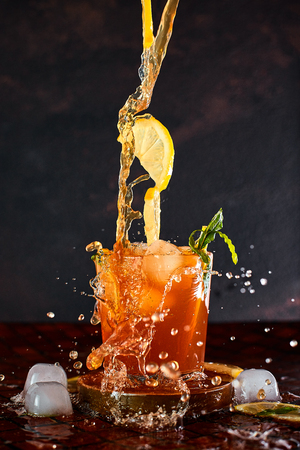 Iced lemon tea on dark background in glass and flying in air ingredients. Levitation effect. Summer cold Iced tea. Food in motion concept. Splashの写真素材