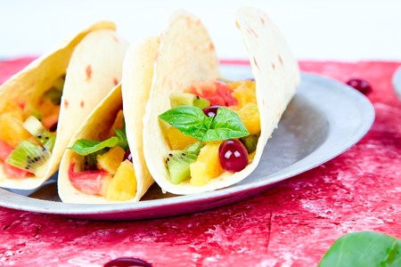 Fruit tacos with orange, kiwi, grapefruit red background and berry. Summer snacks.の写真素材