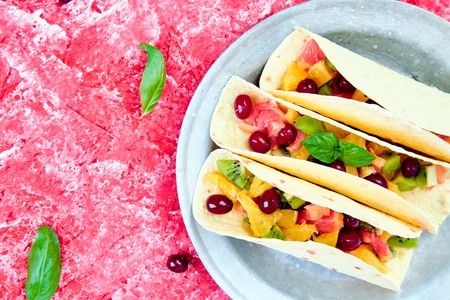 Fruit tacos with orange, kiwi, grapefruit red background and berry. Summer snacks. Top view. Copy space.の写真素材