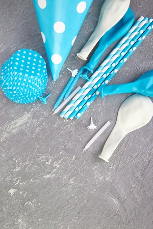 Celebration Flat lay. Party blue hat polka dot on grey background. Birthday paper hat, candles, tubes and balloonsの写真素材