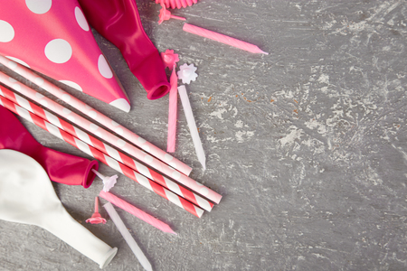 Celebration Flat lay. Party pink hat polka dot on grey background. Birthday paper hat, candles, tubes and balloonsの写真素材