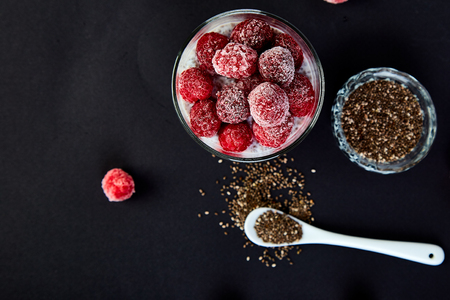 Healthy chia pudding with raspberries in glass on black background. Vegan creamy breakfast. Detox and healthy superfoods breakfast concept. Top view.の写真素材