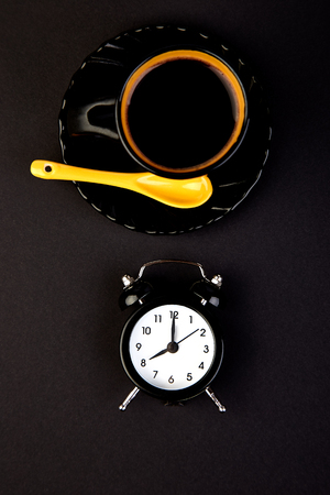 Morning coffee on yellow cup and black alarm clock. Flat lay. Copy space. Top view.の写真素材
