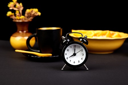 Morning coffee, granola breakfast with fruit near alarm clock, yellow vase flower on black background. の写真素材