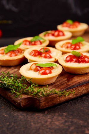 Mini tarts with cherry tomatoes with mozzarella cheese on wooden board.の写真素材