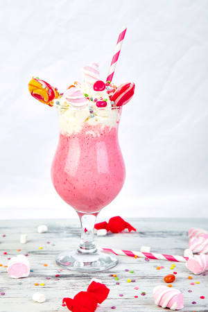 Pink Extreme milkshake with berry, rasberry, strawberry, candy marshmallow, lollipops on white background. Crazy freakshake. Copy space. Food trend. Overshakeの写真素材