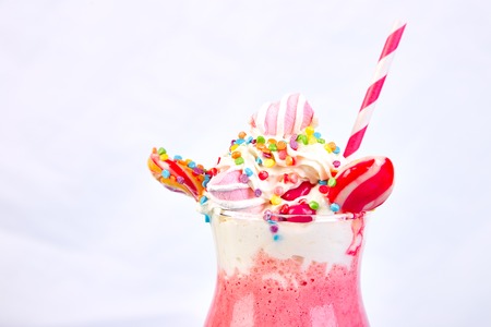 Pink Extreme milkshake with berry, rasberry, strawberry, candy marshmallow, lollipops on blue background.. Crazy freakshake. Copy space. Food trend Overshakeの写真素材