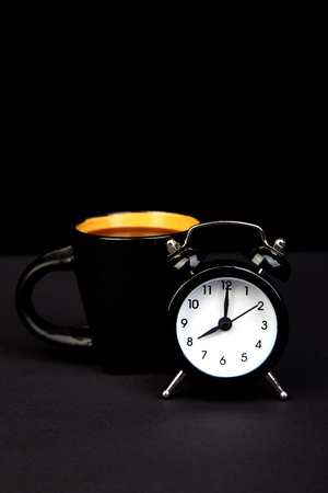 Morning coffee on yellow cup and black alarm clock. の写真素材