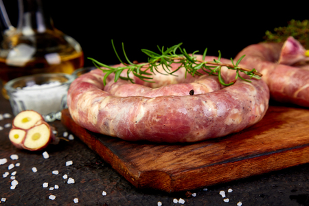 Raw spiral pork sausages with rosemary, salt and peper on wooden cutting board.の写真素材