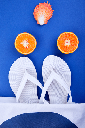 Summer beach bag with white flip flops, seashells, orange fruit on blue background. Flat lay. Top view. Copy space.の写真素材